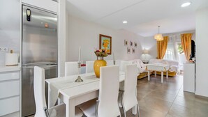Een moderne keuken met een geïntegreerde koelkast, een eettafel met stoelen en een zithoek met een bank en een lamp.