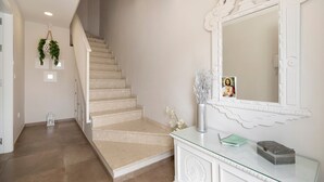 Een trap met beigetint tapijt, een witte muur met een grote spiegel, en een console met glazen blad en decoratieve objecten.