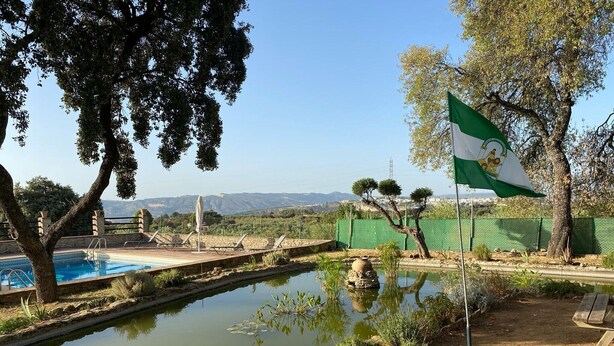 Un espace piscine agrémenté d’un drapeau, de quelques arbres et offrant une vue sur des collines lointaines.
