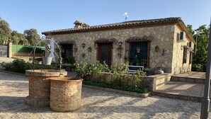 Un bâtiment en pierre avec un toit en tuiles, un petit jardin et une sculpture en métal.