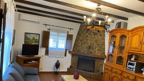 Un salon avec une cheminée en pierre, des meubles en bois, un téléviseur et un lustre.