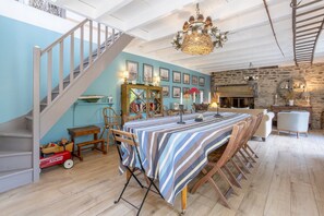 Un coin repas avec une nappe à rayures, des chaises en bois, un lustre et un escalier.