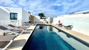 Piscina com espreguiçadeiras, porta de vidro e um salva-vidas vermelho em um dia ensolarado.