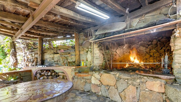 A stone fireplace with a fire, a stone bench, and a rustic wooden ceiling.