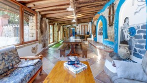A rustic interior with a wooden ceiling, stone walls, a dining table, and a sofa.