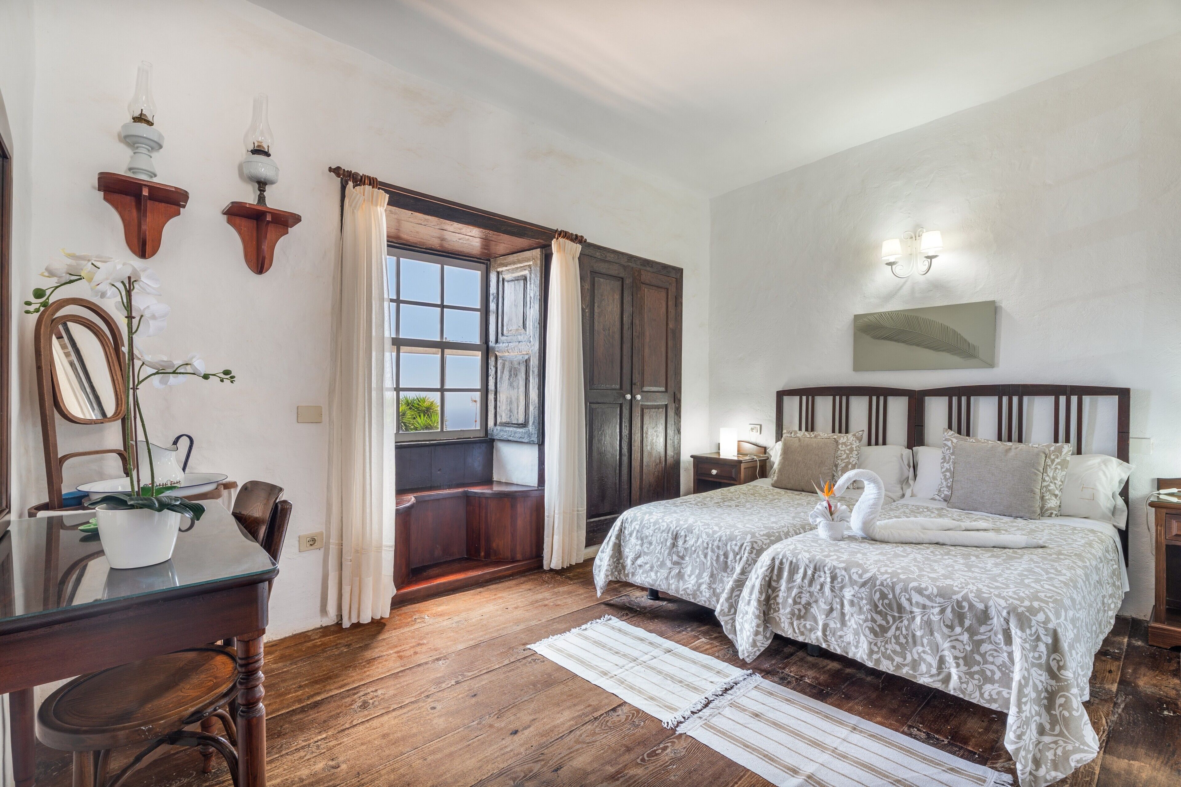 Une chambre à coucher avec un lit double, un bureau avec une chaise, une fenêtre avec des rideaux et un luminaire fixé au mur.