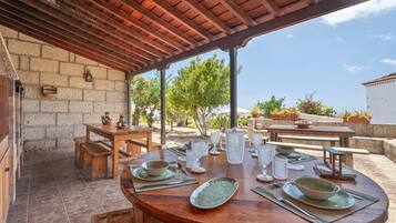 Un patio al aire libre con una mesa de madera dispuesta para comer, rodeado de muros de piedra y plantas en macetas.
