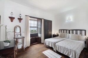 Un dormitorio con dos camas, una ventana con cortinas, piso de madera y una mesita de noche con espejo.