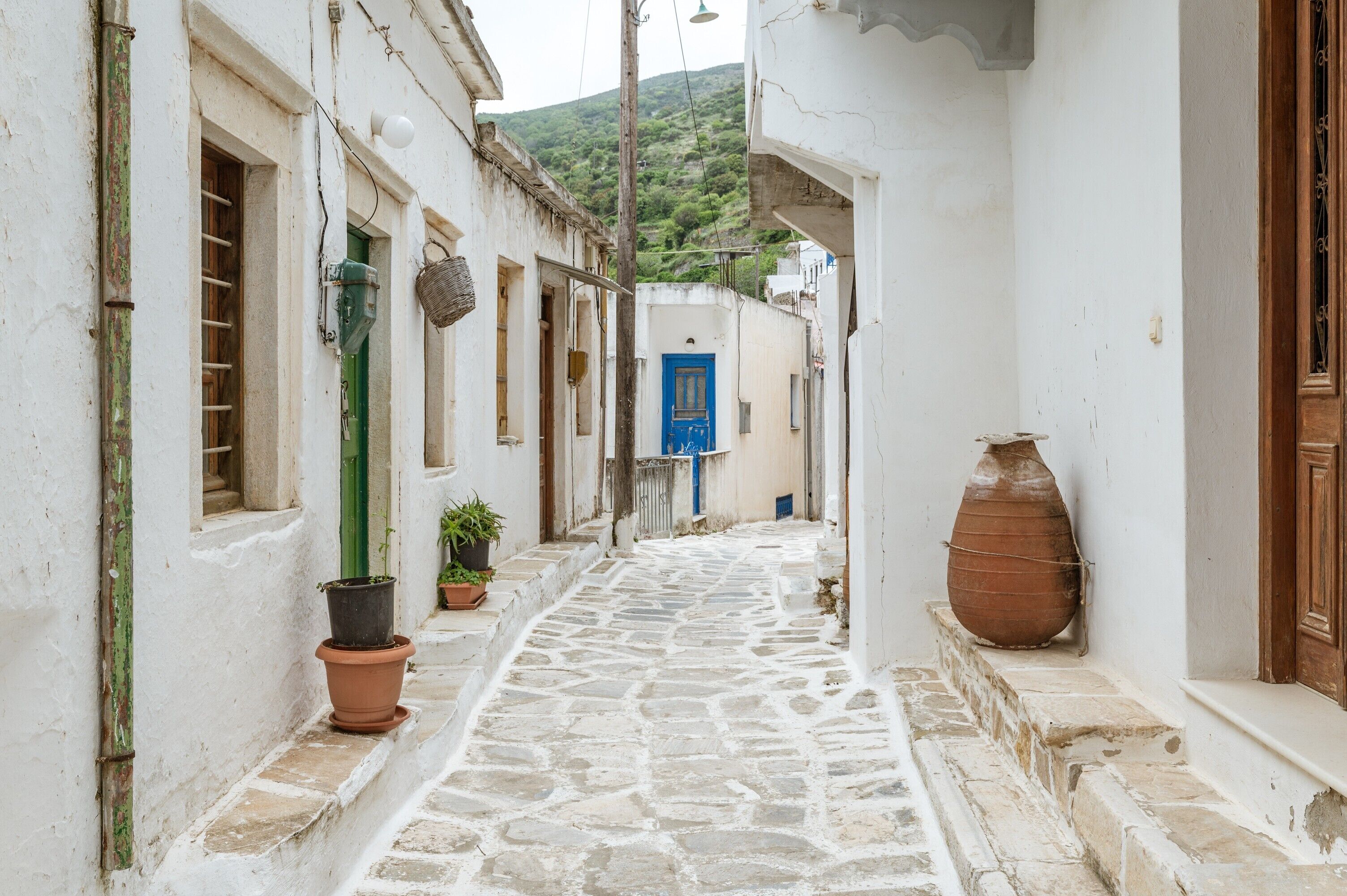 A narrow stone-paved alleyway between white buildings with a blue door in the distance.