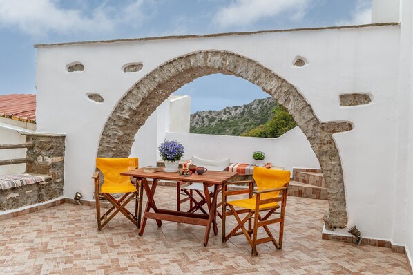 An outdoor patio with a stone archway, a wooden table, and two yellow chairs.