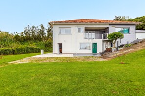 Una casa de dos pisos con techo de tejas rojas, una puerta verde y un pequeño jardín delantero.