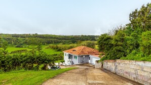 Une maison avec un toit recouvert de tuiles rouges, une allée en béton et un mur en briques sur un de ses côtés.