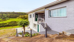 A modern two-story house with a balcony, a green door, and a view of a lush landscape. - Apartment 'Apartamento T2 Praia Do Almoxarife' with Sea View, Wi-Fi and Air Conditioning (Horta)