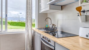 A modern kitchen with a built-in oven, a sink with a dish rack, and a window with a view of greenery. - Apartment 'Apartamento T2 Praia Do Almoxarife' with Sea View, Wi-Fi and Air Conditioning (Horta)