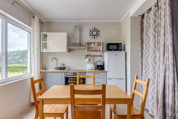 A kitchen with a dining table and chairs, a microwave, a kettle, and a clock on the wall.