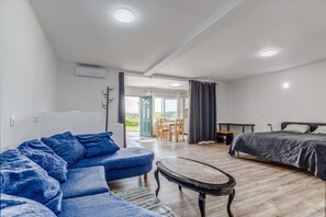 A modern room with a sofa, a bed, a small table, and a view of the outdoors.