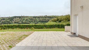 A paved outdoor area with a view of a hilly landscape, a building with a door, and a small garden. - Apartment 'Apartamento T2 Praia Do Almoxarife' with Sea View, Wi-Fi and Air Conditioning (Horta)