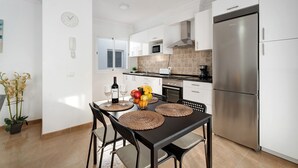 Una cocina moderna con armarios blancos, un refrigerador de acero inoxidable y un comedor con mesa y sillas negras.