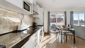 Una cocina moderna equipada con microondas, tostadora y cafetera. Hay un comedor con mesa y sillas, y se ve una vista de edificios desde afuera.