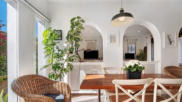 Een eethoek met rieten stoelen, een houten tafel en een hangende lamp.