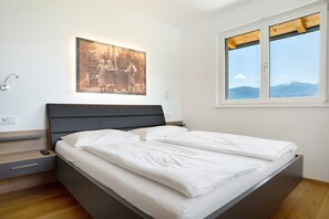 Un dormitorio moderno con cama, mesita de noche, lámpara de pared, cuadro enmarcado y ventana con vistas.