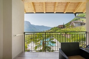 Un balcón con vista a montañas, una piscina y una casa al fondo.