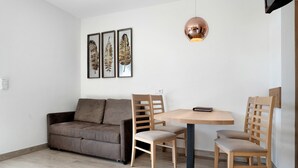 Una sala moderna con un sofá, dos sillones de madera, una mesa redonda e iluminación colgante.