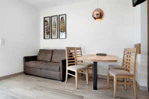 A modern living room with a sofa, two wooden chairs, a round table, and a pendant light.