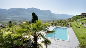 Una piscina con sillas de descanso, rodeada de vegetación y montañas al fondo.