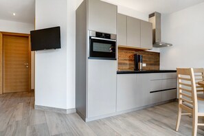 A modern kitchen with built-in appliances, a flat-screen TV, and a dining area with a wooden chair.