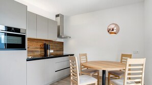 Een moderne keuken met witte kasten, een inbouwoven en een ronde houten eettafel met vier stoelen.