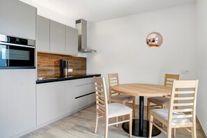 A modern kitchen with white cabinets, a built-in oven, and a round wooden dining table with four chairs.