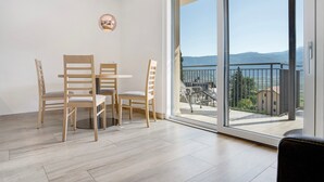 Een moderne kamer met een eettafel en stoelen, een grote schuifdeur naar een balkon met uitzicht op bergen en een meer.