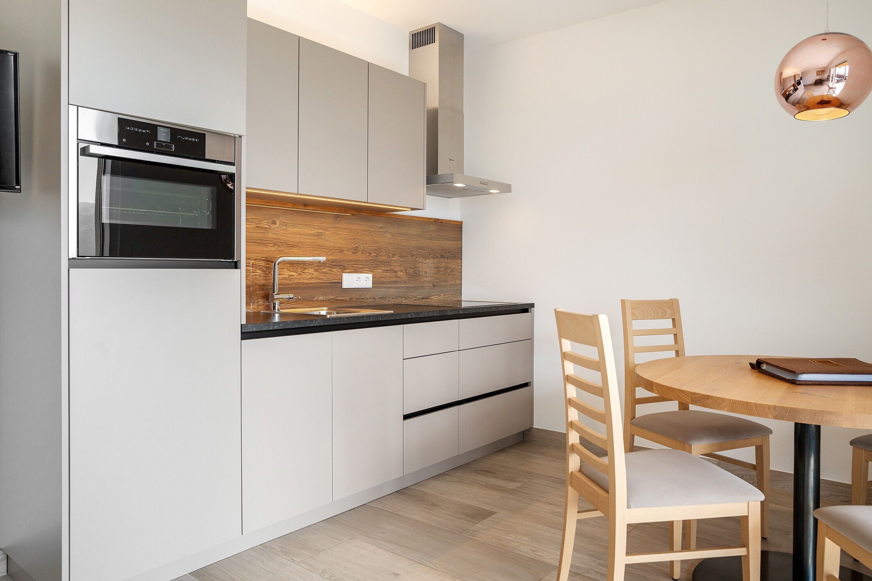 Eine moderne Küche mit Einbauofen, einer Holz Arbeitsplatte und einem Essbereich mit rundem Tisch und Stühlen.