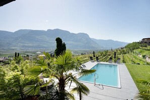 Piscina com espreguiçadeiras, cercada por vegetação e montanhas ao fundo.