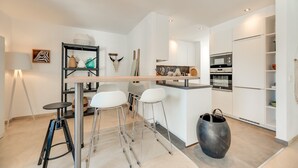 Uma cozinha moderna com armários brancos, uma ilha central, banquetas e uma panela grande.