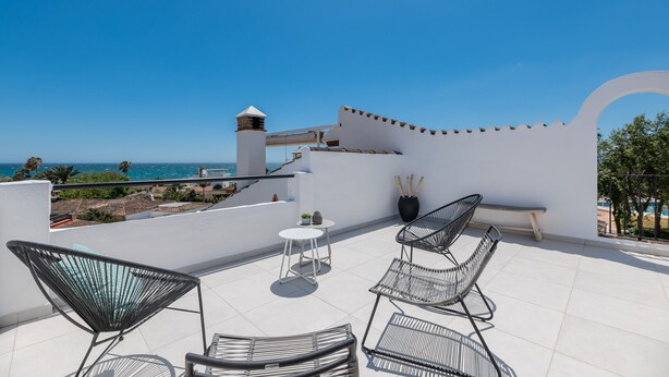Terraço no terraço com vista para o mar, apresentando uma parede branca, uma chaminé e cadeiras de metal preto.