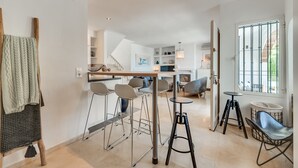 Uma cozinha moderna com banquetas, área de jantar com cadeiras, escada e janela com grades.