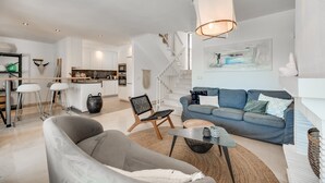 Uma sala de estar moderna com um sofá, uma mesa de centro e uma poltrona. Há uma escada que leva a um andar superior.