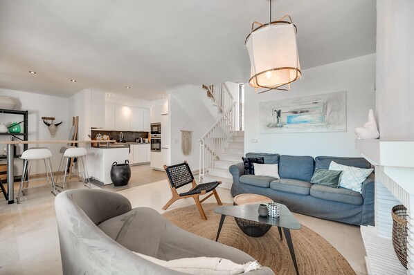 A modern living room with a sofa, a coffee table, and a chair. There is a staircase leading to an upper level.