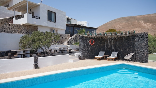 A modern pool area with a stone wall, lounge chairs, and a clear blue pool. - 'Finca La Calerita C' with Sea View (Yaiza)