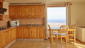 A kitchen with wooden cabinets, a microwave, a sink, and a dining area with chairs and a table. - 'Finca La Calerita C' with Sea View (Yaiza)