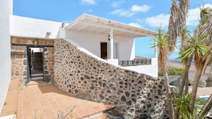 A stone-walled building with a white exterior, a tiled patio, and a view of the sea. - 'Finca La Calerita C' with Sea View (Yaiza)