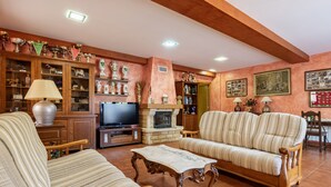 Een woonkamer met een bank, fauteuils, een televisie, een open haard en een kast met trofeeën.