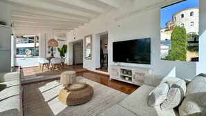A spacious living area with a large flat-screen TV, a dining table with chairs, and a cozy seating area with a woven ottoman.