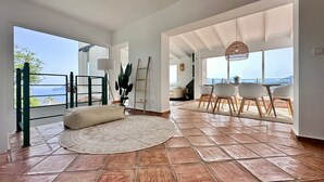 A spacious living area with a large window, a round rug, and a dining set.