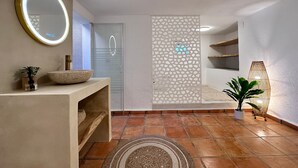 A bathroom with a round mirror, a bowl sink, a decorative panel, a potted plant, and a textured rug.