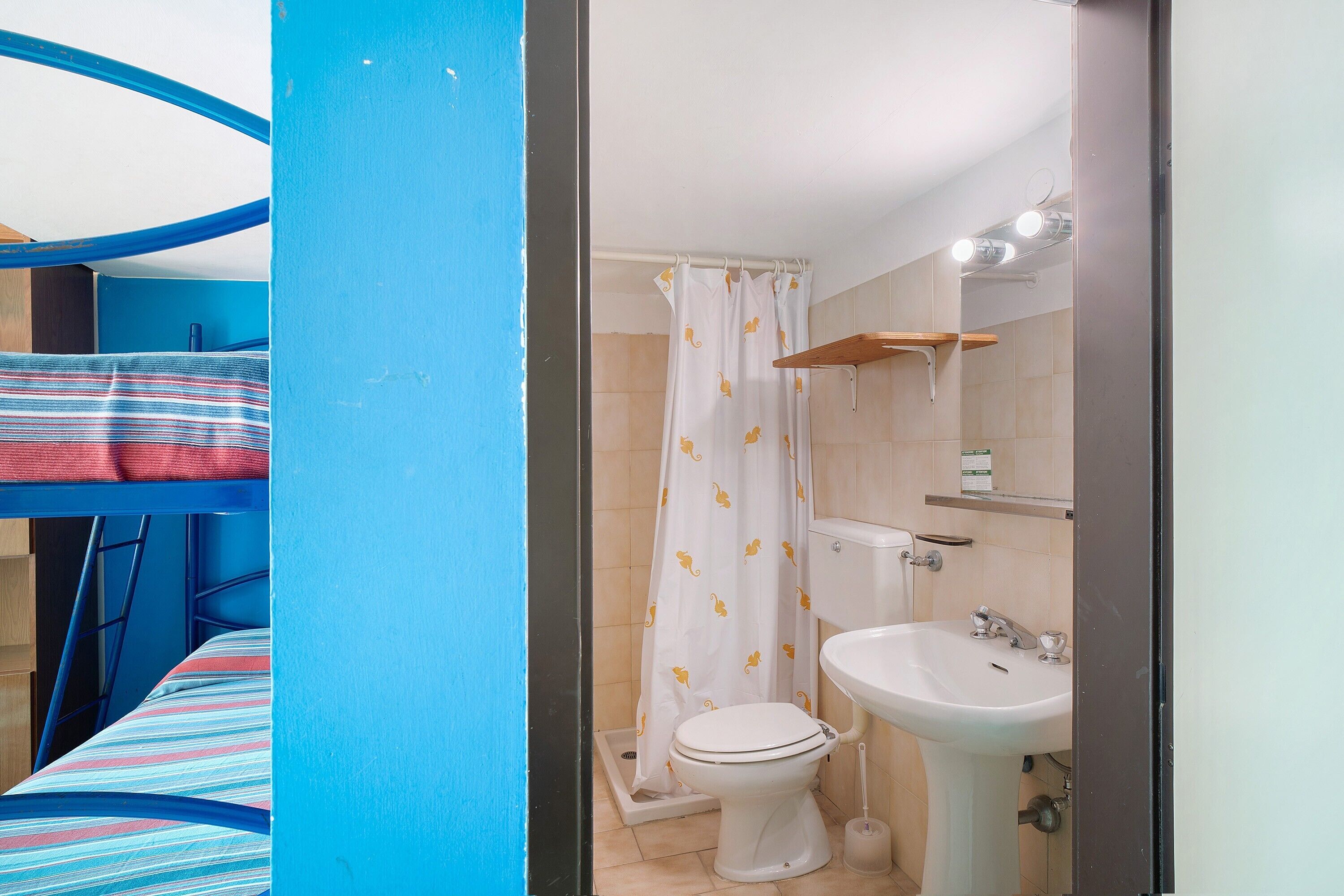 A bunk bed with a striped bedspread, a shower with a yellow pattern curtain, a white sink, and a mirror above it.