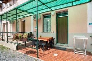 Un espacio al aire libre cubierto con una mesa, sillas, una planta en maceta y una mesa blanca independiente.