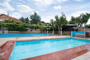 Una piscina con cubierta de madera, rodeada de vegetación y una cerca.